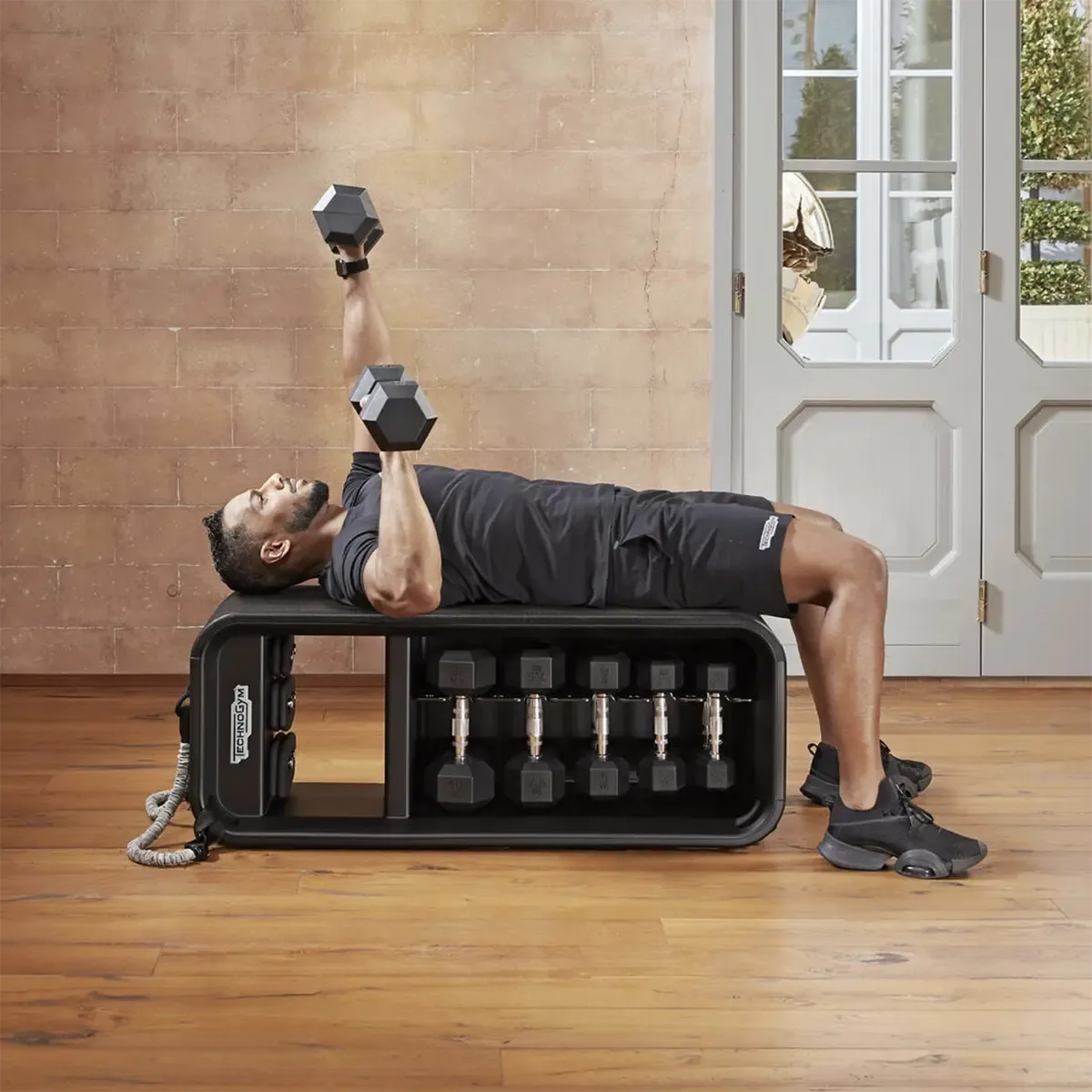 Technogym Home workout bench with dumbbells, elastic bands, and weighted knuckles
